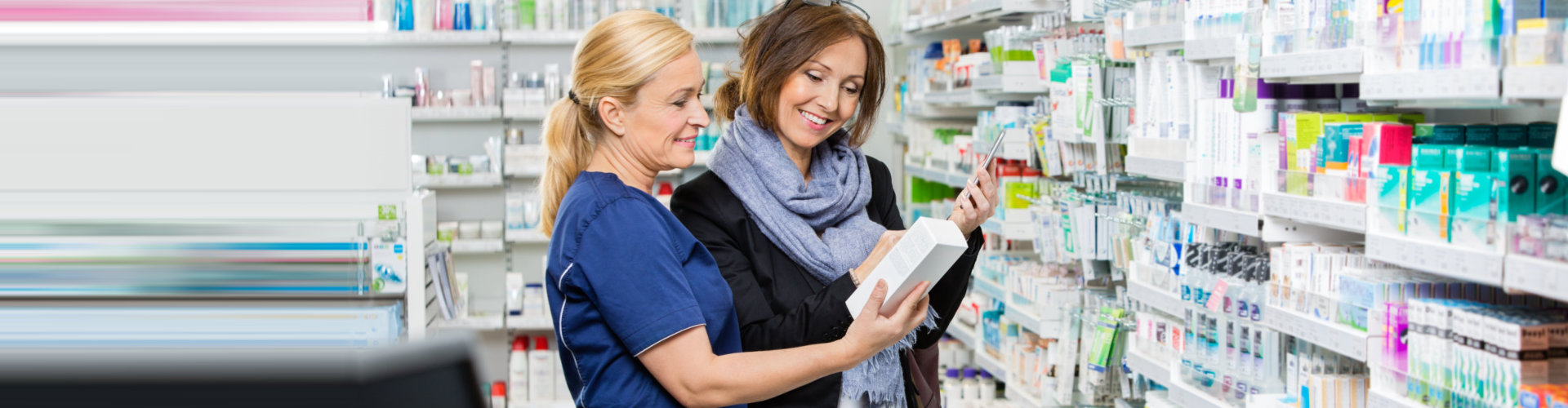 female pharmacist in blue uniform and female customer looking at the medicine box